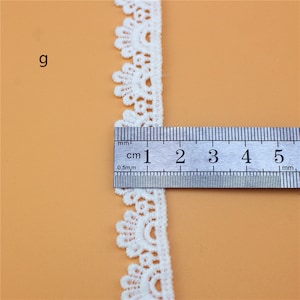 May include: White lace trim with a scalloped edge, measuring approximately 2 cm wide. The trim is shown next to a ruler.