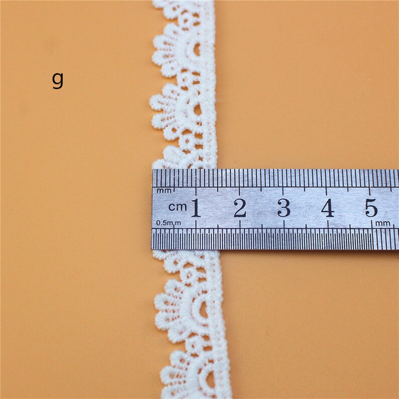 May include: White lace trim with a scalloped edge, measuring approximately 2 cm wide. The trim is shown next to a ruler.