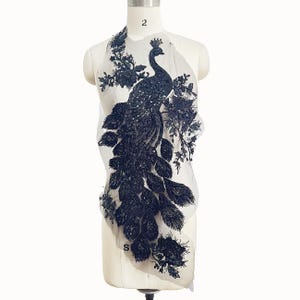 May include: Black beaded peacock applique with a detailed design. The applique is on a sheer fabric background.