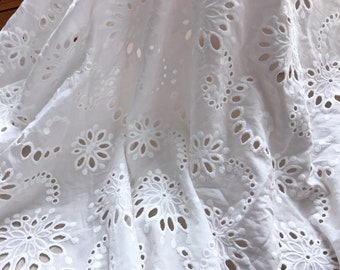 May include: White cotton fabric with a delicate eyelet pattern. The fabric has a soft, airy feel and is perfect for creating summery garments or home decor.