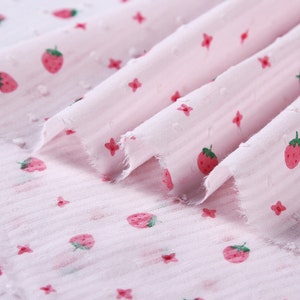 May include: Pink fabric with a white polka dot pattern and a repeating strawberry print.