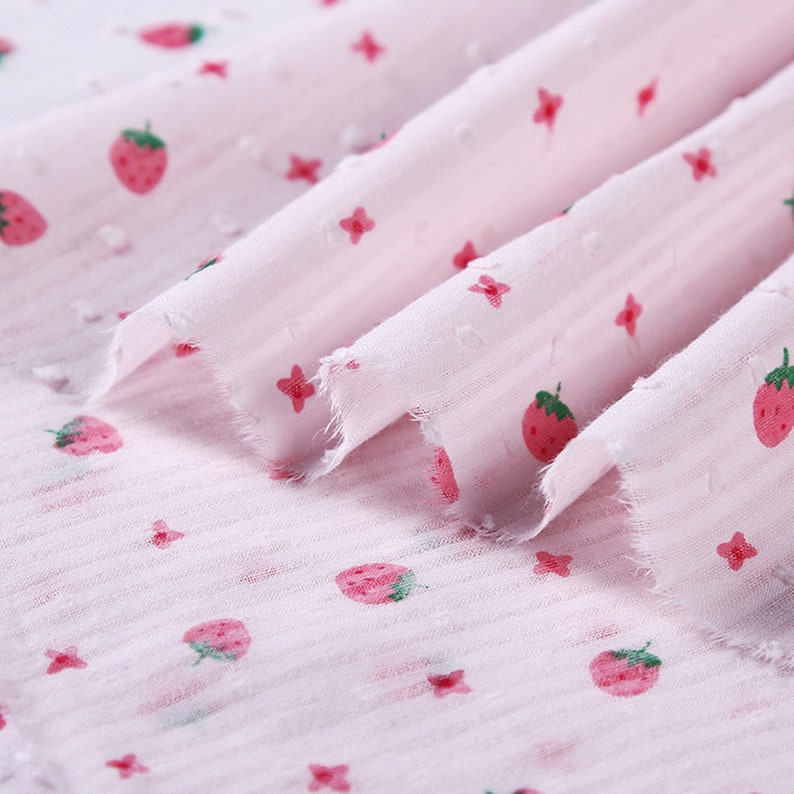 May include: Pink fabric with a white polka dot pattern and a repeating strawberry print.