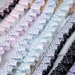 Può includere: Primo piano di diverse file di nastri arricciati in vari colori pastello, tra cui rosa, lavanda e blu. Ogni nastro è adornato da piccoli pois neri. I nastri sono disposti in linee parallele, creando un motivo visivamente accattivante.