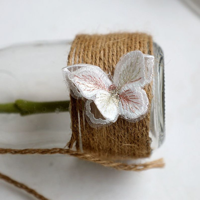 May include: A glass jar wrapped in brown twine with a white lace butterfly embellishment.