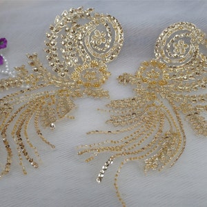 May include: Two gold-coloured fabric appliques with a floral design. The appliques are made of sequins and beads and have a delicate, intricate pattern.