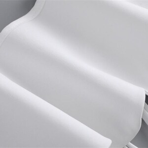 K&ouml;nnte beinhalten: Nahaufnahme eines wei&szlig;en Stoffes mit R&uuml;schendesign. Der Stoff ist gefaltet und drapiert, wodurch weiche Schatten und Glanzlichter entstehen. Die Textur erscheint glatt und die Gesamt&auml;sthetik ist sauber und elegant. Das Bild deutet auf ein Kleidungsst&uuml;ck oder Textil hin.