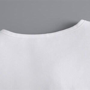 K&ouml;nnte beinhalten: Nahaufnahme des Ausschnitts eines wei&szlig;en T-Shirts. Das Shirt besteht aus einem glatten, blickdichten Stoff. Der Ausschnitt ist ein einfaches, abgerundetes Design mit einem d&uuml;nnen, gen&auml;hten Rand. Der Hintergrund ist einfarbig grau.