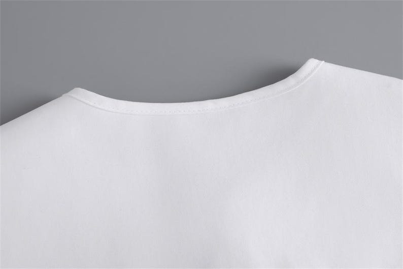 K&ouml;nnte beinhalten: Nahaufnahme des Ausschnitts eines wei&szlig;en T-Shirts. Das Shirt besteht aus einem glatten, blickdichten Stoff. Der Ausschnitt ist ein einfaches, abgerundetes Design mit einem d&uuml;nnen, gen&auml;hten Rand. Der Hintergrund ist einfarbig grau.