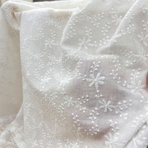 Puede incluir: Una tela blanca transparente que presenta un intrincado patr&oacute;n bordado de peque&ntilde;as flores y delicados tallos similares a enredaderas. El material ligero tiene una textura suave con un motivo floral repetitivo cosido en hilo blanco.