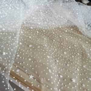 May include: White tulle fabric with a white polka dot and star pattern.