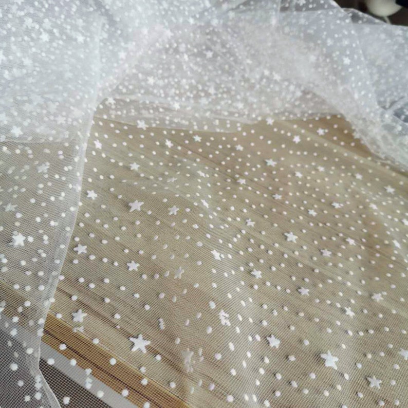 May include: White tulle fabric with a white polka dot and star pattern.