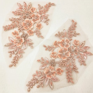 Pode incluir: Dois delicados apliques florais cor de pêssego com detalhes em pérolas e lantejoulas. Os apliques estão em um tecido de malha transparente e apresentam desenhos florais intrincados.