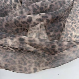 Könnte beinhalten: Nahaufnahme eines transparenten Stoffes mit Leopardenmuster. Der Stoff ist eine Mischung aus Braun, Beige und Schwarz, wobei das Tiermuster sichtbar ist. Der Stoff ist drapiert und erzeugt Falten und Schatten.