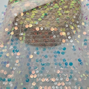 Puede incluir: Tela de lentejuelas iridiscentes con un respaldo de malla blanca transparente. Las lentejuelas son de varios colores, incluyendo azul, verde y dorado. La tela es adecuada para crear vestidos, disfraces o acentos decorativos.