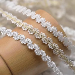 Puede incluir: Tres galones de encaje blancos con diferentes patrones. Los galones tienen un diseño floral delicado con un brillo sutil.