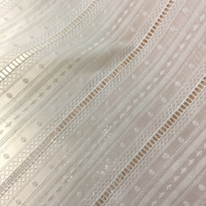 May include: White fabric with a delicate, embroidered pattern featuring a repeating geometric design. The fabric has a subtle sheen and a slightly textured surface.