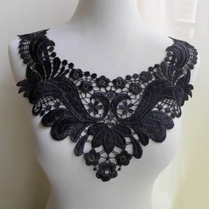 May include: Black lace trim featuring a delicate floral design. The trim is shaped like a V-neck and would be ideal for adding a touch of elegance to a garment.
