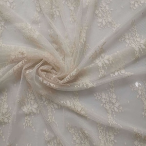 May include: White lace fabric with a delicate floral pattern. The fabric is sheer and has a soft, flowing texture.