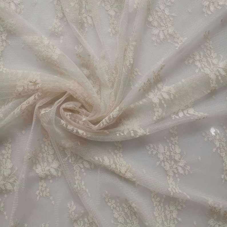 May include: White lace fabric with a delicate floral pattern. The fabric is sheer and has a soft, flowing texture.
