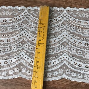 May include: White lace trim with a scalloped edge and a repeating floral pattern. The trim is approximately 1.5 inches wide.