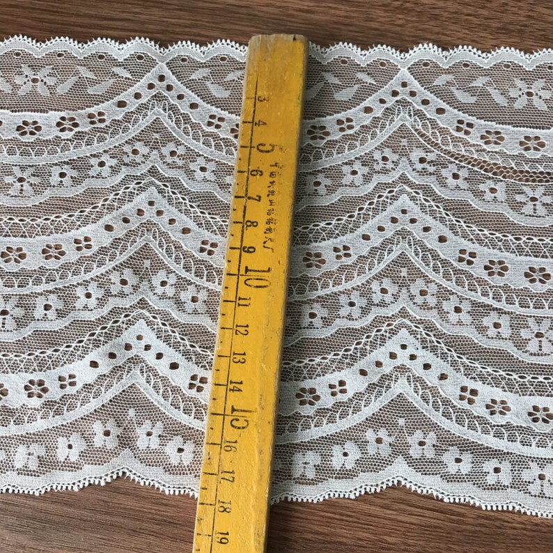 May include: White lace trim with a scalloped edge and a repeating floral pattern. The trim is approximately 1.5 inches wide.