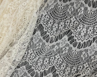 May include: Close-up of two sections of lace fabric. One section is a creamy off-white, and the other is a bright white. The lace has an intricate floral and geometric pattern, with delicate openwork and a textured surface. The fabric is draped.