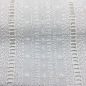 May include: White cotton fabric with an intricate embroidered pattern. The design features repeating geometric shapes and small circles.