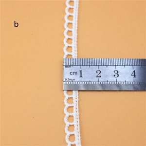May include: White crochet trim with a scalloped edge, measured against a ruler showing 4 centimeters.