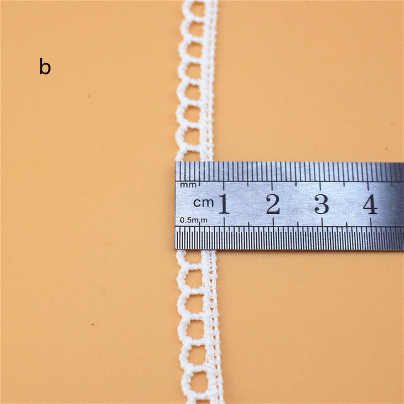 May include: White crochet trim with a scalloped edge, measured against a ruler showing 4 centimeters.