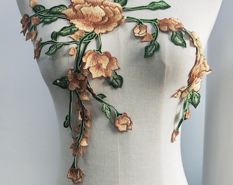 May include: Embroidered floral applique in shades of orange and green, displayed on a mannequin. The design features a large central flower with cascading vines and smaller blossoms. Perfect for embellishing garments or crafts.