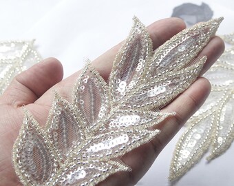 May include: A delicate, beaded and sequined leaf applique with a sheer mesh backing. The applique is in a light gold color with clear sequins.