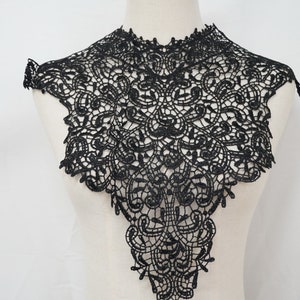 Op de afbeelding: Zwarte kantversiering met een delicaat bloemenpatroon. De versiering is kraagvormig en heeft een puntige onderkant.