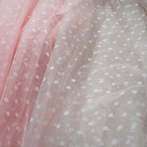 Puede incluir: Dos capas de tela transparente con lunares blancos. La capa superior es de color rosa claro y la capa inferior es blanca.