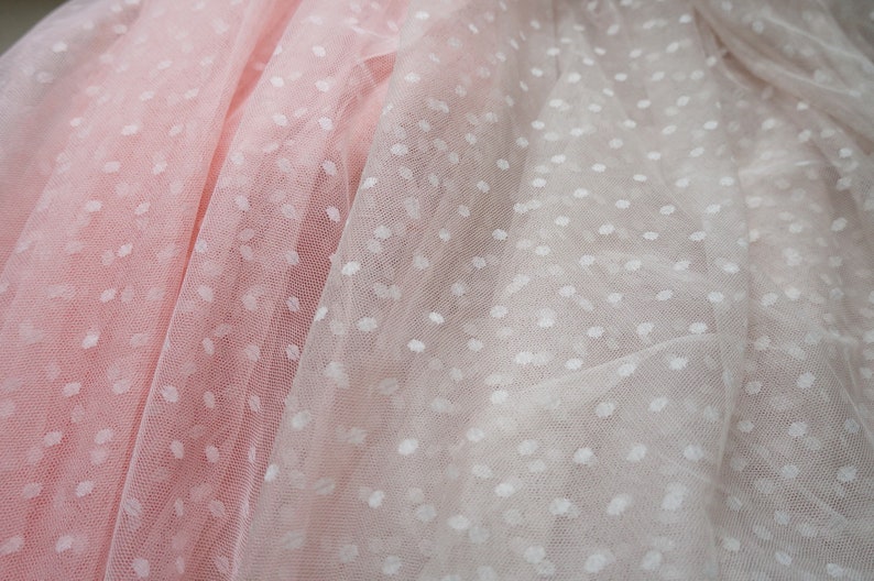 Puede incluir: Dos capas de tela transparente con lunares blancos. La capa superior es de color rosa claro y la capa inferior es blanca.