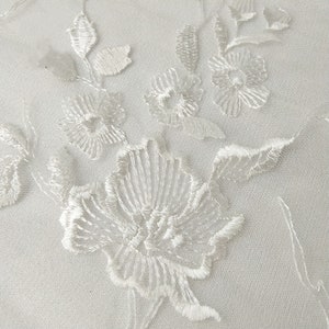 K&ouml;nnte beinhalten: Wei&szlig;er Blumenspitzenstoff mit einem zarten Stickmuster. Die Spitze zeigt ein sich wiederholendes Muster aus kleinen Blumen und Bl&auml;ttern.