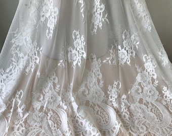 May include: White floral lace fabric with a scalloped edge. The lace is delicate and intricate, with a floral pattern throughout. The fabric is sheer and lightweight, making it perfect for a variety of projects.