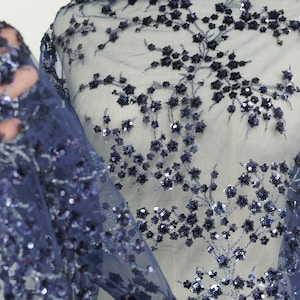 Puede incluir: Tela azul marino transparente con un patrón floral hecho de lentejuelas. Las lentejuelas están dispuestas en un diseño delicado e intrincado.