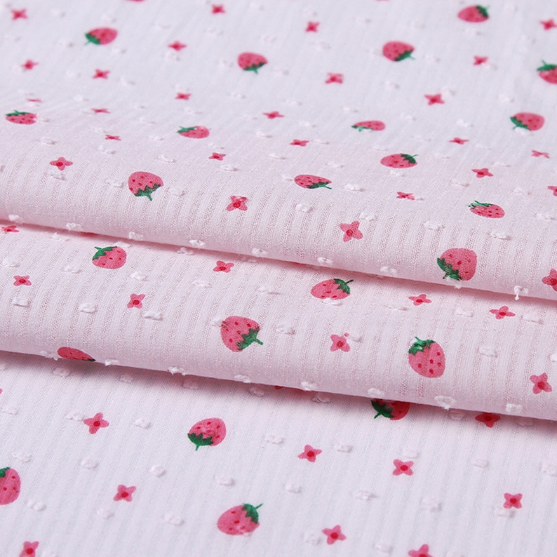 May include: Pink fabric with a white polka dot pattern and a repeating strawberry print.