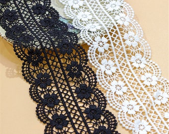 Puede incluir: Dos carretes de encaje delicado, uno negro y uno blanco. El encaje presenta un borde festoneado con un patrón floral repetitivo.