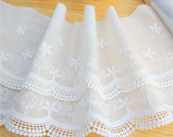 Könnte beinhalten: Weißer Baumwollspitzenbesatz mit einem gewellten Rand und kleinen weißen Blumen, die durchgehend gestickt sind. Die Spitze hat einen zarten, femininen Look und wäre perfekt, um jedem Projekt einen Hauch von Eleganz zu verleihen.