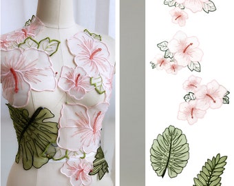 Könnte beinhalten: Ein Set aus rosa und grünen gestickten Blumenapplikationen. Die Applikationen zeigen Hibiskusblüten und Blätter. Die Applikationen sind perfekt, um jedem Projekt einen Hauch von tropischem Flair zu verleihen.