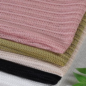 Puede incluir: Primer plano de una pila de telas de punto en varios colores. Los colores incluyen rosa, verde oliva, beige, negro y blanco. El material de punto tiene un tejido delicado y abierto.