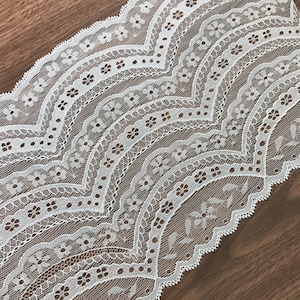 May include: White lace trim with a scalloped edge and a delicate floral pattern.