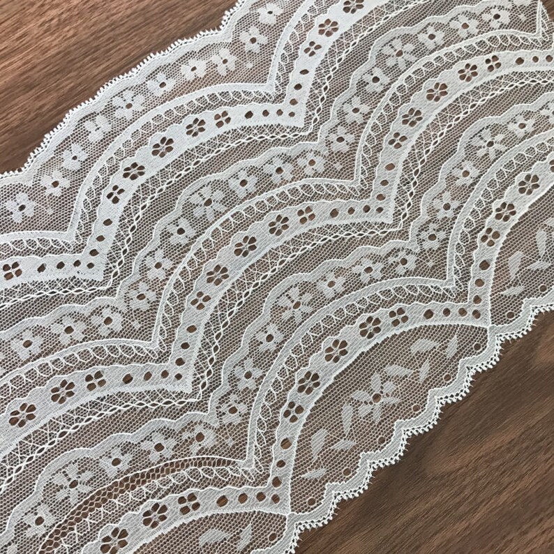 May include: White lace trim with a scalloped edge and a delicate floral pattern.