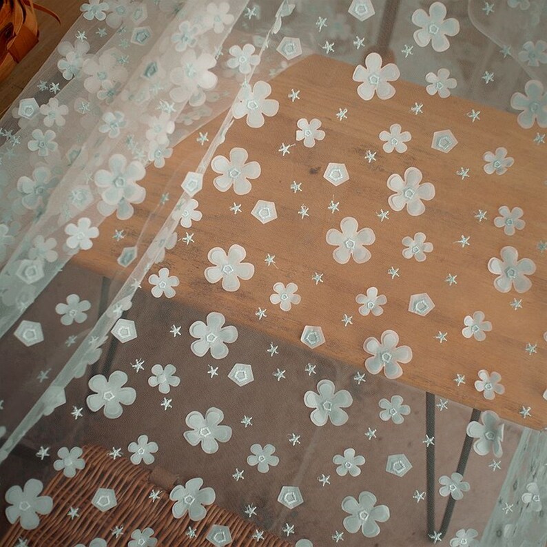 May include: White sheer fabric with a light blue floral pattern. The fabric is decorated with small flowers and stars.