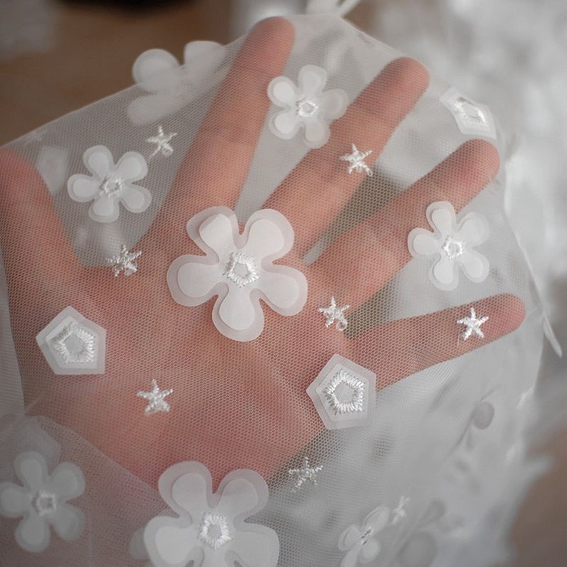 May include: White sheer fabric with embroidered white flowers and stars.