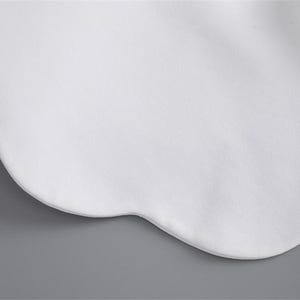 K&ouml;nnte beinhalten: Nahaufnahme eines wei&szlig;en Kragens mit wellenf&ouml;rmigem Rand. Der Kragen besteht aus einem weichen, glatten Stoff und hat eine abgerundete Form. Wei&szlig;e B&auml;nder sind auf der rechten Seite des Bildes zu sehen. Der Hintergrund ist einfarbig grau.