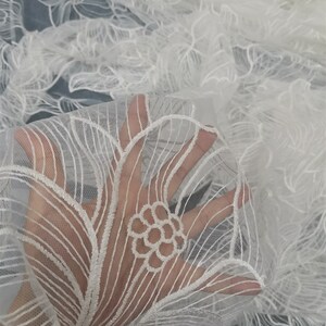 May include: White floral lace fabric with a delicate embroidered design. The lace is sheer and has a soft, flowing texture.