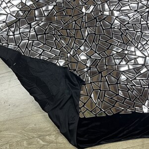K&ouml;nnte beinhalten: Schwarzer Stoff mit einem silbernen, spiegelnden Mosaikmuster. Der Stoff hat eine weiche, samtige Textur.