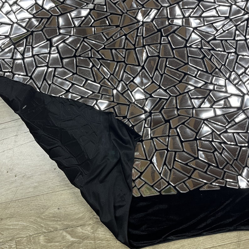 K&ouml;nnte beinhalten: Schwarzer Stoff mit einem silbernen, spiegelnden Mosaikmuster. Der Stoff hat eine weiche, samtige Textur.